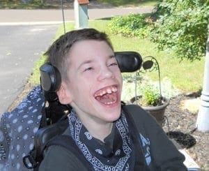 Young person in a wheelchair laughs heartily outdoors.
