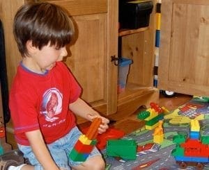 Child in red shirt plays with colorful building blocks on a mat.