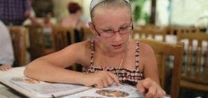 Girl in glasses points to a menu at a restaurant table.