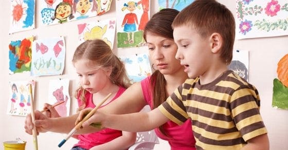 Children and an adult paint at an art class with artwork displayed on the wall.