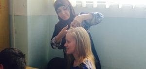 A woman braids another woman's hair.