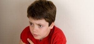 Young boy in a red shirt clutches his arm and looks away.