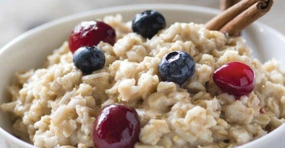 Bowl of oatmeal with blueberries, cherries, and cinnamon sticks.