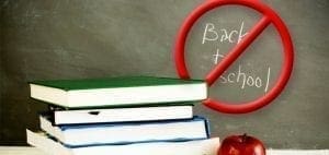 Stack of books with a red "no" symbol over the words "Back to school" written on a chalkboard.