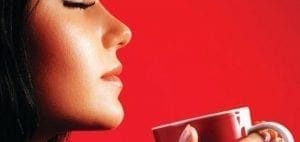 Woman with eyes closed holding a red mug.