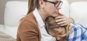 Woman with glasses comforts a distressed teen.