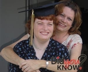 A smiling graduate wearing a cap and gown is embraced by a woman.