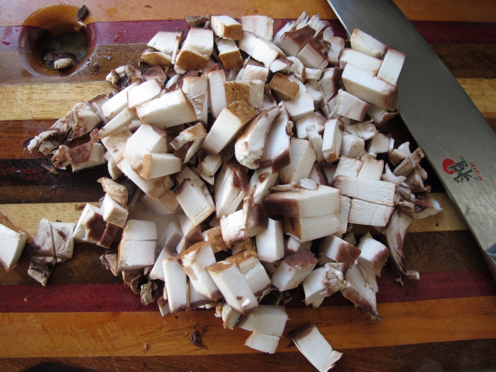 Pile of diced mushrooms on a cutting board next to a knife.