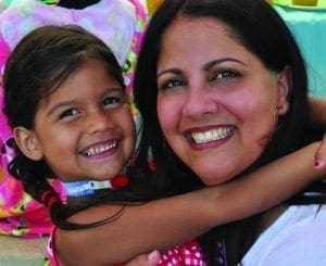 A woman smiles while hugging a young girl, who has her arm around the woman.