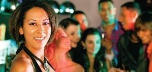 A woman smiles at the camera with a group of people in the background at a party.