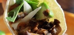 Mushroom taco with avocado, onion, and cilantro in a corn tortilla.