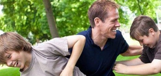 A father laughs with his two sons outdoors.