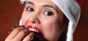 Woman in Santa hat eats a chocolate pastry.