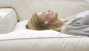 Woman lying on her side with eyes closed on a white couch.