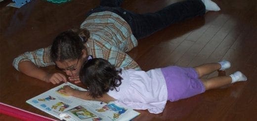 Two people lie on a wooden floor looking at a book.
