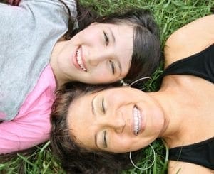 Two smiling women lying down on grass.