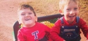Two smiling children in red shirts and overalls in a wagon.
