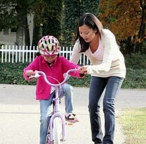 A woman helps a child learn to ride a bicycle.