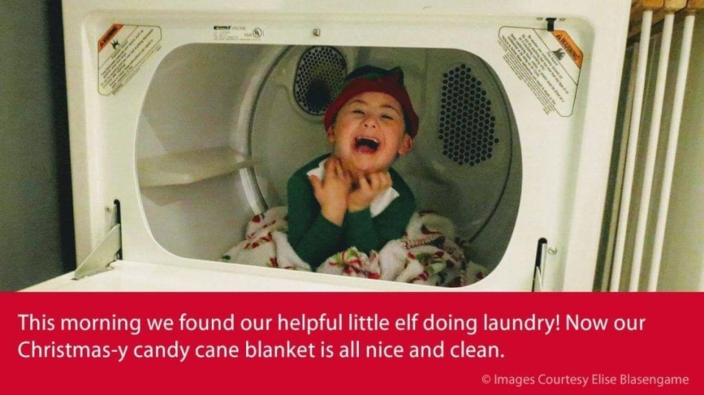 A child in an elf hat sits in a dryer, laughing.