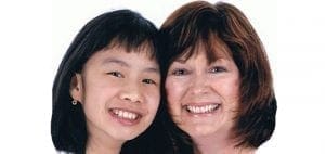 Two smiling women, one Asian child and one adult Caucasian woman, pose together.