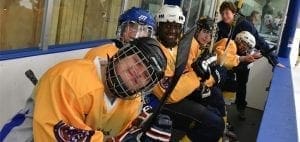 Hockey players in yellow jerseys with helmets and sticks on a bench.