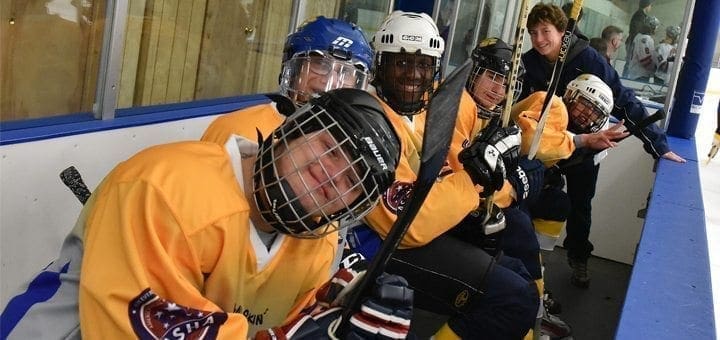 Hockey players in yellow jerseys with helmets and sticks on a bench.