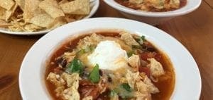 Bowls of chicken tortilla soup topped with sour cream and tortilla chips, served with a side of tortilla chips.