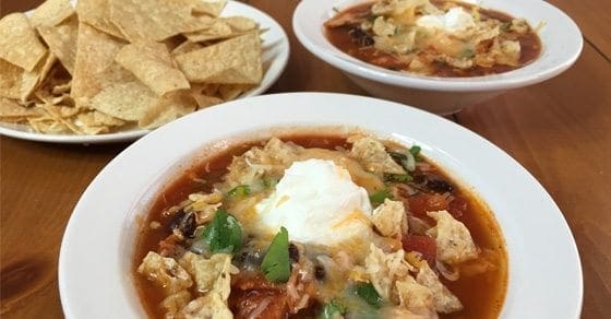 Bowls of chicken tortilla soup topped with cheese and a side of tortilla chips.