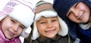 Three children smiling while wearing winter hats.