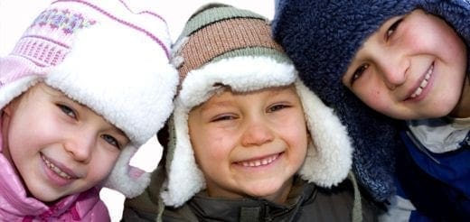 Three children smiling while wearing winter hats.