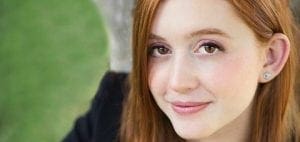 A young woman with red hair smiles.