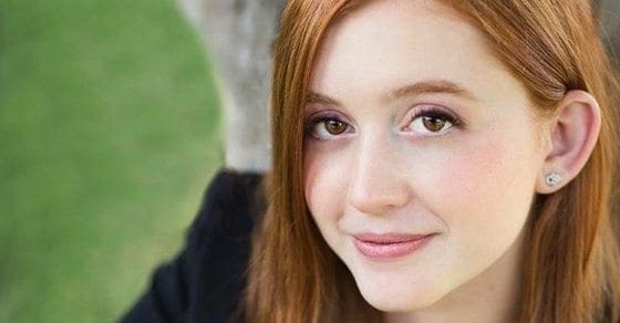Young woman with red hair smiles outdoors.