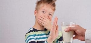Boy covers mouth and holds up hand to refuse a glass of milk.