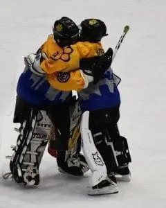 Two hockey players in full gear hugging on the ice.