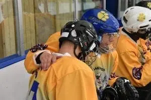 Two hockey players in yellow jerseys and helmets embrace on the ice.