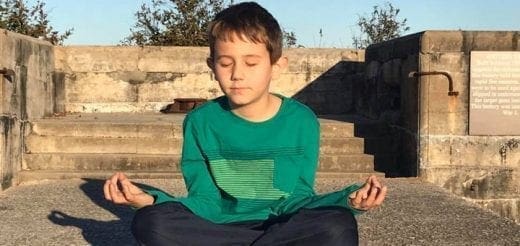 Boy meditating in a cross-legged pose outdoors.