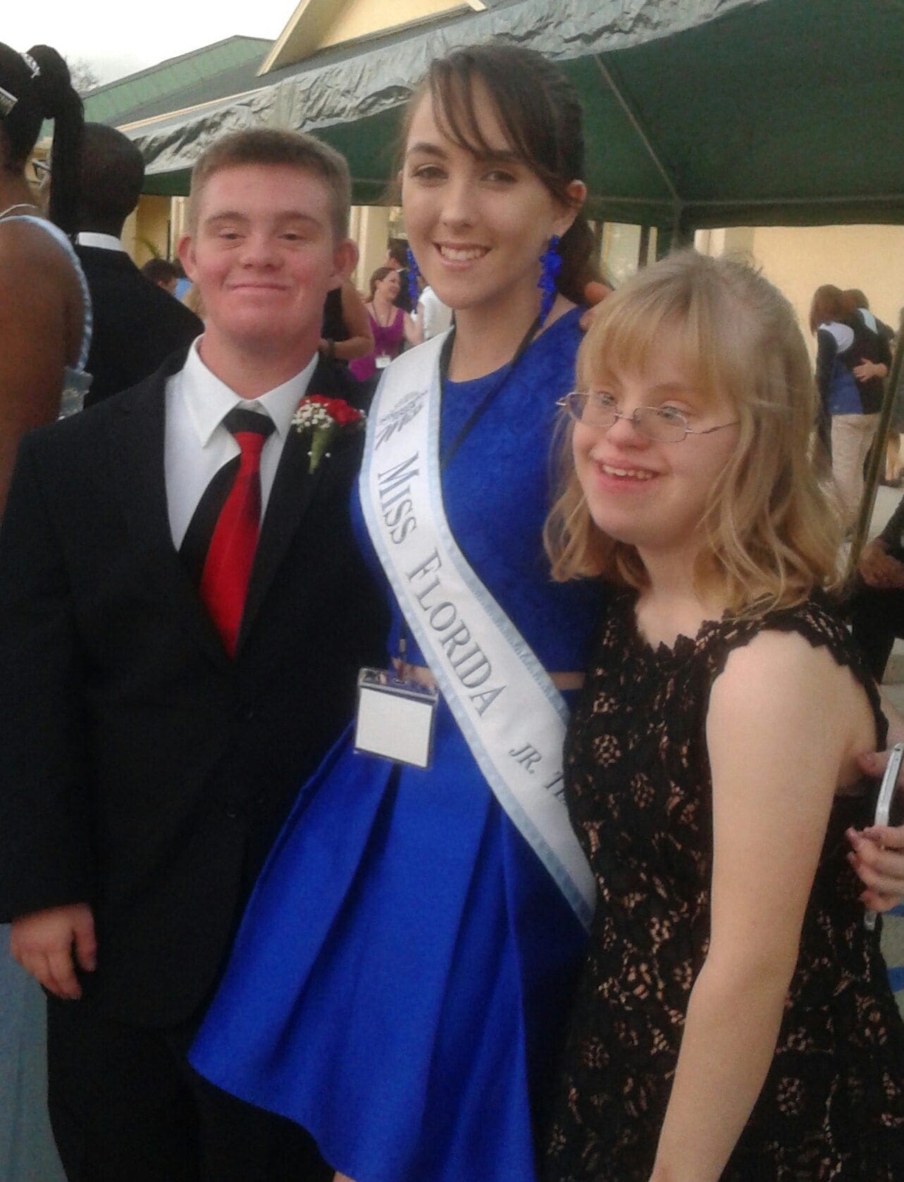 Three people pose for a photo, two wearing formal attire and one wearing a "Miss Florida" sash.