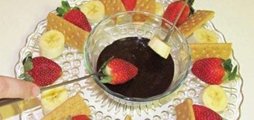 Chocolate fondue with strawberries, banana slices, and crackers on a decorative plate.