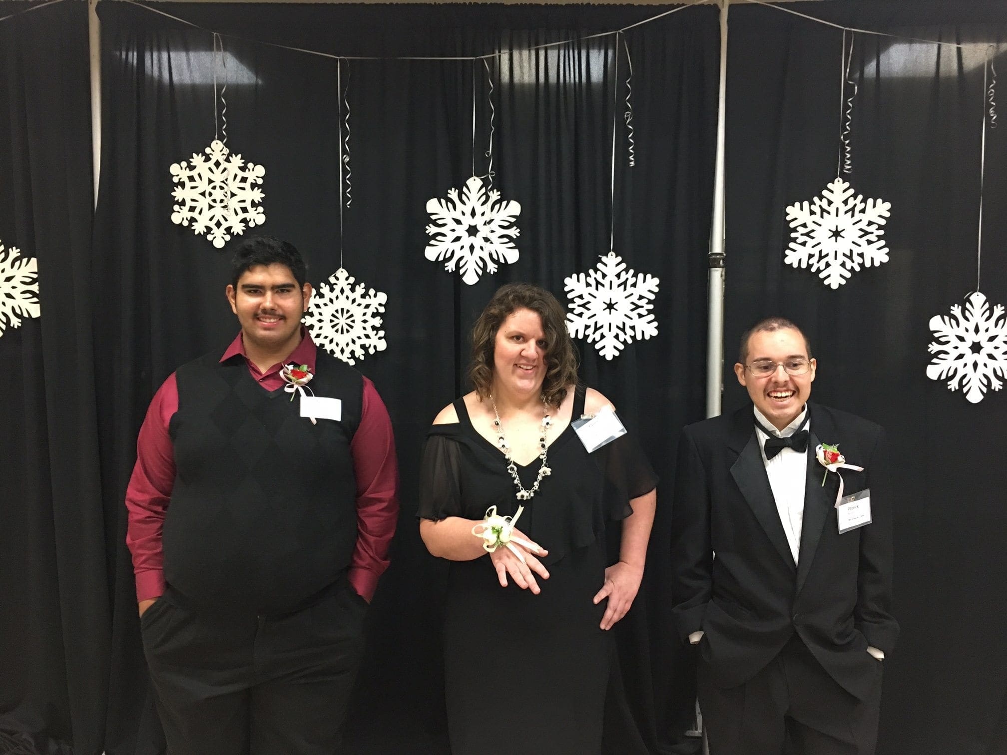 Three people posing in front of a black backdrop with snowflake decorations.