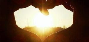 Hands forming a heart shape against a sunset.