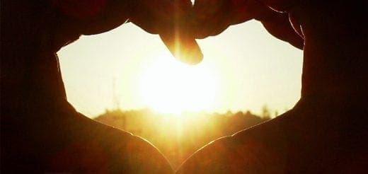 Hands forming a heart shape against a sunset.