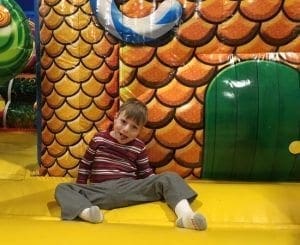 Boy in striped shirt sitting in front of an inflatable play structure.