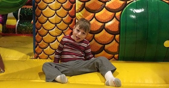 Boy sitting on a yellow floor in an inflatable play structure.