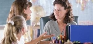 A teacher talks with a student and another adult in a classroom setting.