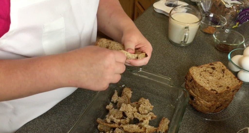Person tearing bread into pieces over a baking dish.