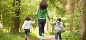 Woman holding hands with two children walking in a forest.