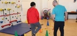 A physical therapist guides a child through an obstacle course.