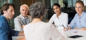 Five professionals seated around a table during a meeting.