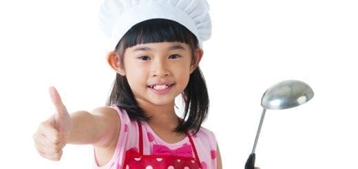 Girl in chef hat and apron gives thumbs up, holding a ladle.