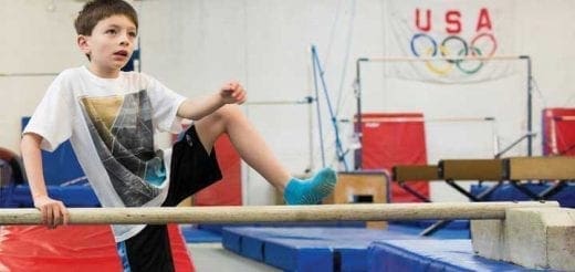 Young boy practicing gymnastics on a bar in a gym.